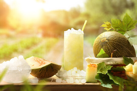 Natural melon drink with ice on wooden table in field