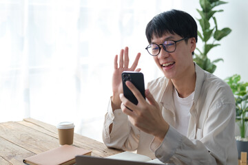 Asian man in casual clothing making facetime video calling with smartphone at home.