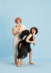Portrait of two women in image of innocent angel and emotional devil on blue background. Models in...