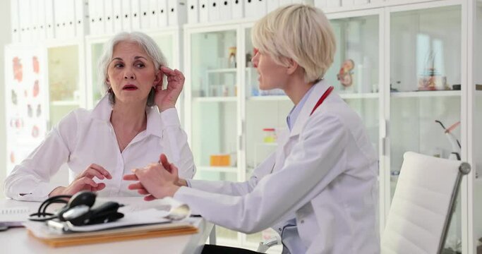 Elderly woman puts hand to ear trying to hear words of doctor. Specialist explains treatment plan for patient with hearing problems slow motion