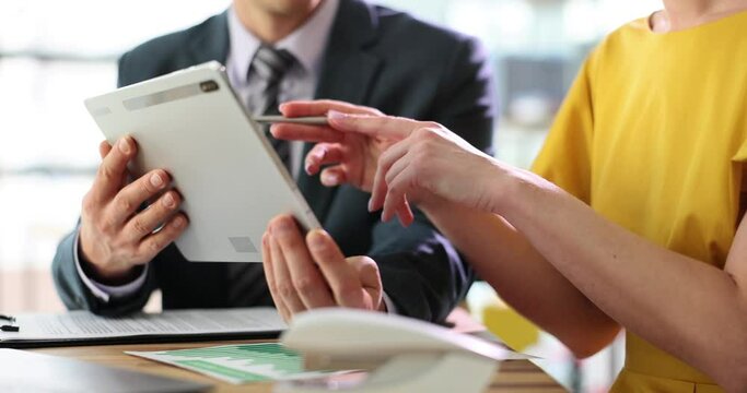 Woman explains project tasks to colleague demonstrating data on tablet in office. Manager gives instructions to young employee at workplace