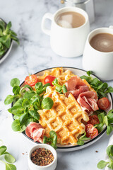 Cheesy belgian waffles served with ham, tomatoes and lettuce corn on white marble background . Savory waffles. Healthy breakfast