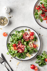 Green salad with ham or prosciutto, corn salad leaves, tomatoes and cheese. Healthy diet lunch on white marble background top view flat lay