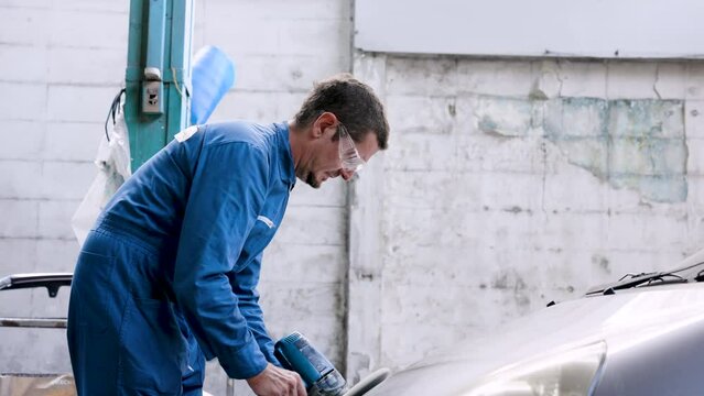 Hand male mechanic wearing suit for working in garage for safety in risky work, wear dustproof goggles, mechanic standing using polishing machine scrub surface car that comes garage make new color.