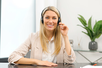 Naklejka premium Headshot of friendly charming caucasian woman in headset, smiling at camera while working in the customer service department as call center operator, providing consultations on the phone