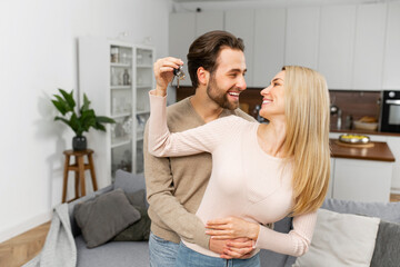 Happy young caucasian married couple holding key ring in hand, hugging and looking at each other...