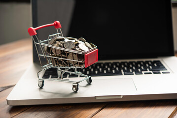 coin in mini shopping cart on table for work and laptop for work to shopping online concept © photobyphotoboy