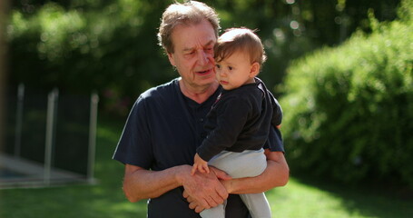 Fototapeta premium Senior man holding infant baby outside. Grand father bonding with toddler outdoors