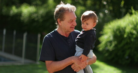 Senior man holding infant baby outside. Grand father bonding with toddler outdoors