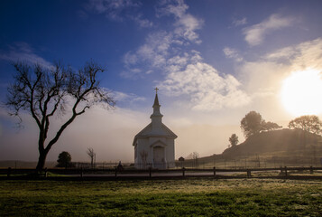 Early morning sun, mist, and fog on small rural church in field