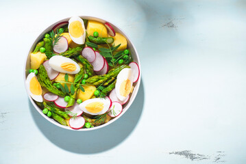 Fototapeta na wymiar Hot spring salad with asparagus, boiled potatoes, radishes, fresh green peas, bacon, and farm eggs. Fresh spring recipes with asparagus, balanced healthy food