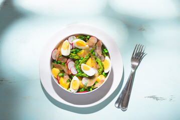 Hot spring salad with asparagus, boiled potatoes, radishes, fresh green peas, bacon, and farm eggs. Fresh spring recipes with asparagus, balanced healthy food