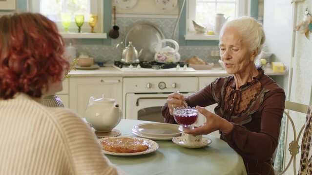 Over-the-shoulder selective focus shot of unrecognizable young woman spending tea time with her granny, grandmacore concept