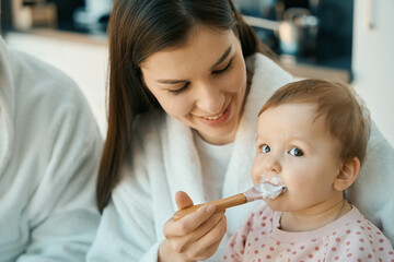 Happy female feeds the baby with a small spoon