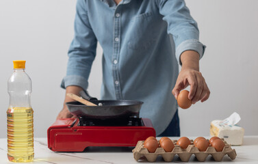 Man's hand picks up an egg to fry in a pan.