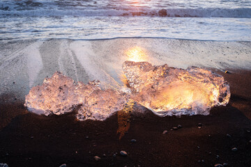 Pure Ice Shining on Black Volcanic Sand at Sunset. Icebergs from Glacier in Sun Rays. Clear Ice in Ocean Waves. Famous Tourist Location in North Europe Country. Travel Destination Diamond Beach..