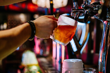 man bartender hand at beer tap pouring beer in glass in bar or pub