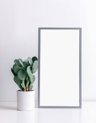 A mock-up of an interior poster with a vertical empty wooden gray frame standing on a table, with potted cacti on the sides, against a white wall.Generative AI