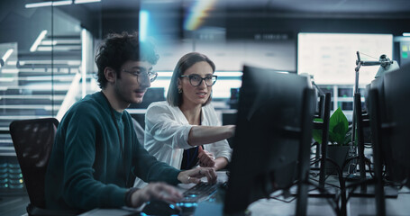 Two Young Colleagues Working on Computers and Talking at a Workplace. Female and Male Software Developers Discussing a Solution for Their Collaborative Artificial Intelligence Project