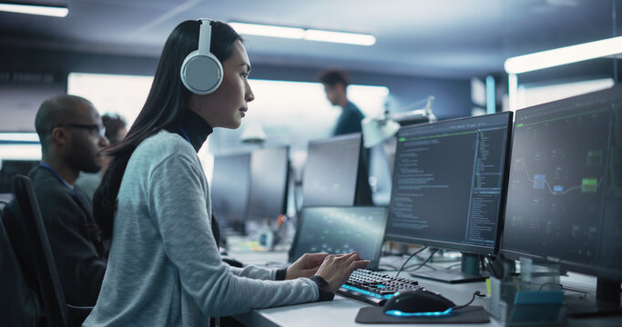 Portrait of a Thoughtful Young Engineer Working on Computer in a Technological Office Environment. Beautiful Asian Woman Wearing Headphones, Writing Software Code for a Blockchain Project