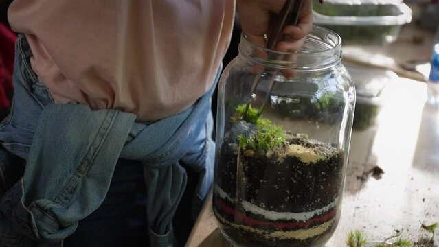 Person making terrarium. Group of people at outdoor florarium training and seminar. Self-sustaining micro garden ecosystem. People learning to create terrariums. Zen meditation hobby. Creative meetup.