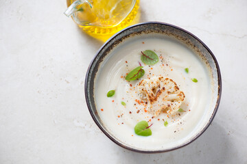 Bowl of cauliflower cream-soup on a light-beige stone background, elevated view, horizontal shot