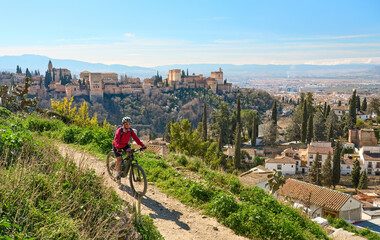 nice active senior woman cycling with her electric mountain bike in Granada below the world heritage site of Alhambra, Granada, Andalusia,  Spain - obrazy, fototapety, plakaty