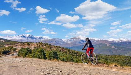 Fototapeta premium nice, active senior woman cycling with her electric mountain bike below the snow covered mountains of the Spanish Sierra Nevada, near Granada, Andalusia, Spain