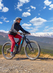 nice, active senior woman cycling with her electric mountain bike below the snow covered mountains of the Spanish Sierra Nevada, near Granada, Andalusia, Spain