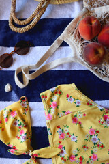 Fototapeta premium Floral bikini, sunglasses, straw bag, seashell and tote with peaches on striped beach towel. Top view.