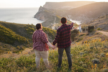 Tourists: a guy and a girl on top of a mountain watching a beautiful sunset. Travel and active life concept.