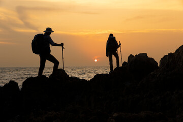 Silhouette Man and woman hiker , trekking on rock along sea side