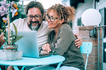 Happy serene couple in love using laptop together at home in the garden smiling and having fun. Man...