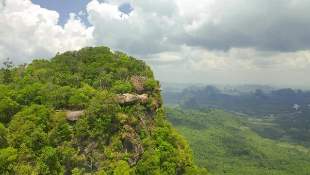 A tourist sits on the cliff edge overhanging the plain on clouds day. Dragon's Crest - Khao Ngon Nak on Krabi Province, Thailand.