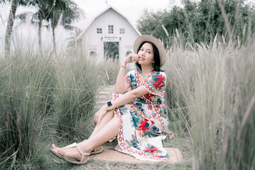 Asian woman sitting in the middle of white grass with a wooden barn in the background
