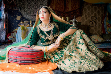 A young woman dressed in Indian ceremonial attire. was sitting leaning against a large pillow staring at something.
