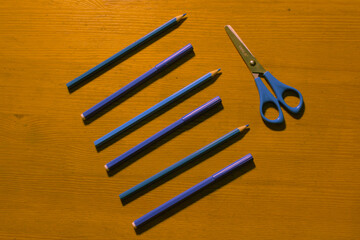 line of blue pencils and blue scissors on a wooden background