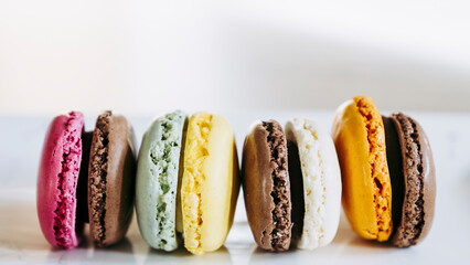 Assortiment de macarons colorés au chocolat framboise orange vanille citron alignés - Arrière plan coloré patisserie française	