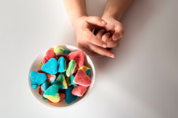 Child hands holds a bowl with colorful sour and sweet candies on a white background.