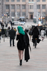 Obraz premium A woman with a perfect figure and red lips in a short black dress, a bright scarf on her head. Posing in the city