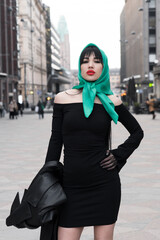 A woman with a perfect figure and red lips in a short black dress, a bright scarf on her head. Posing in the city