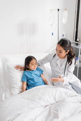 Obraz premium asian pediatrician showing hand to little girl sitting on hospital bed.