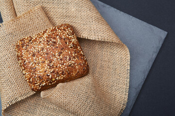 One freshly baked rustic square shaped bread loave with sesame seeds on the vintage rustic country style sackcloth grey stone plate and solid fond plain black background