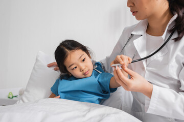 little asian child touching stethoscope near pediatrician in hospital ward.