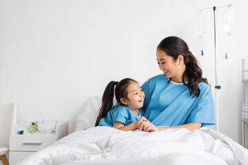 young asian woman holding hands of smiling daughter on bed in hospital ward.