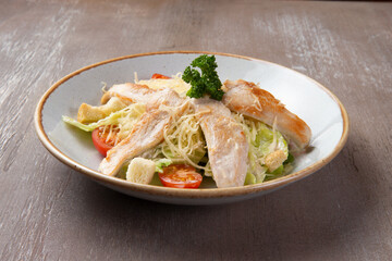 Salad with chicken fillet in a plate on a brown background.