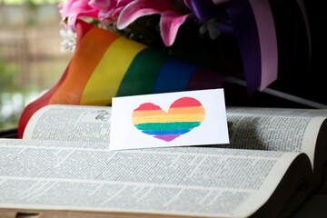 Closeup view of bookmark in heart shape which drew with rainbow colours, blurred opened old book...