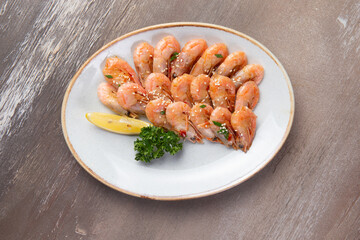 Cooked shrimp and lemon in a plate on a brown background.