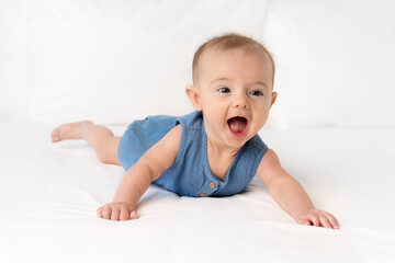 Happy young baby with open mouth lying on stomach on white bed