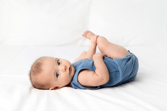 Side view of newborn baby lying on white bed looking at camera